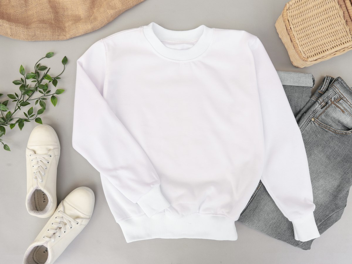 White crew-neck sweatshirt laid flat with sneakers
